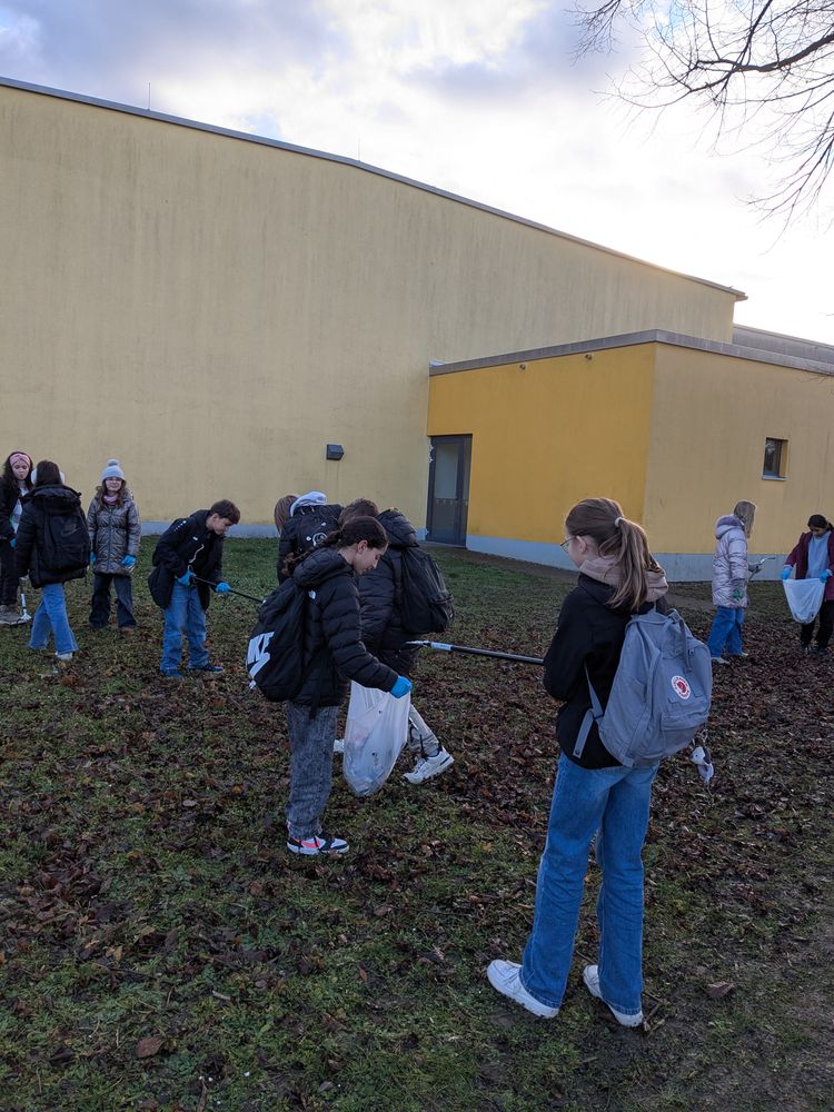 Schülerinnen sammeln hinter der Sporthalle Müll ein